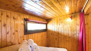 Una stanza con rivestimento in legno, un letto, una finestra con tenda rossa e un lampadario a parete.