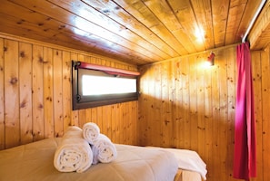 A wooden-paneled room with a bed, a window with a red curtain, and a wall-mounted light fixture.