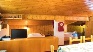 Interno di una baita in legno con una televisione su un tavolo di legno, due letti e una sveglia appesa al muro.