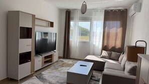Uma sala de estar moderna com televisão de tela plana, um sofá, uma mesa de centro e uma janela grande com cortinas.