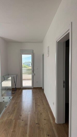 Um quarto com piso de madeira, uma mesa de vidro e uma porta que dá para uma varanda.
