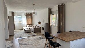 Una cocina moderna con encimera de madera y taburetes de bar, un comedor con mesa y sillas, un sofá y un refrigerador pequeño.