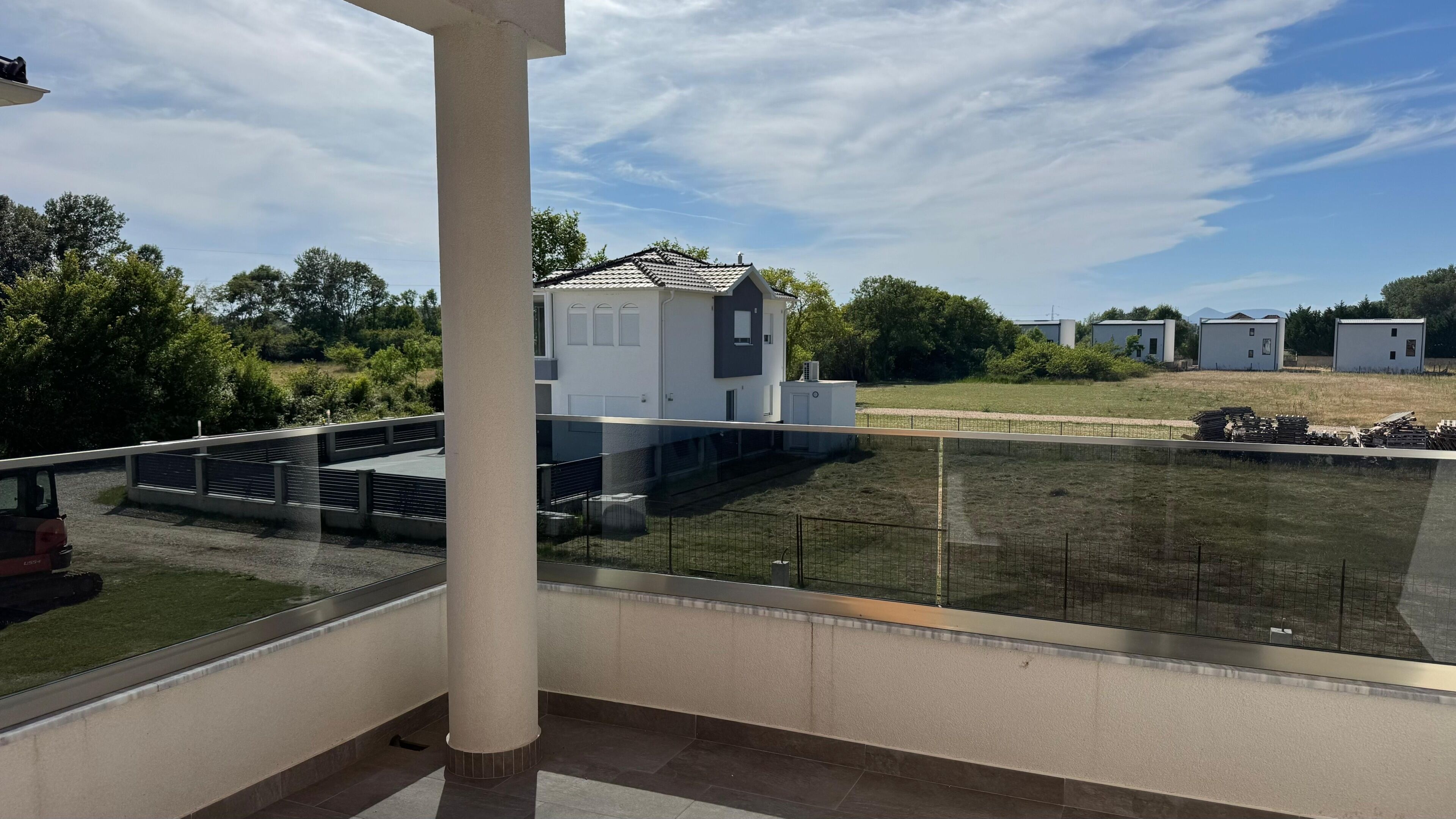 Ein Balkon mit Blick auf ein modernes Gebäude, einen eingezäunten Bereich und einen klaren Himmel.