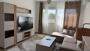 Ein modernes Wohnzimmer mit Flachbildfernseher, einer Couch, einem Couchtisch und einer Lampe.