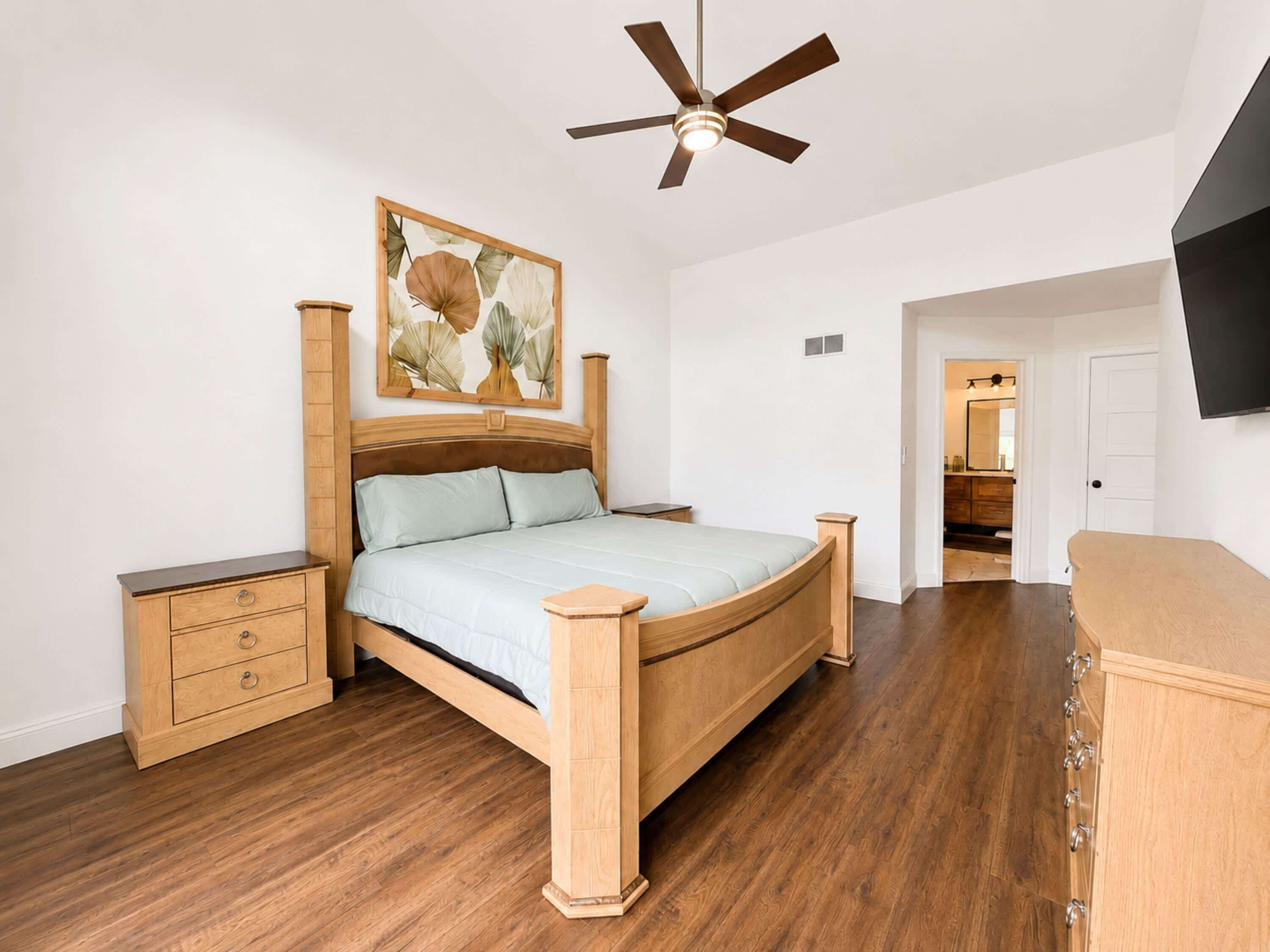 A bedroom with a wooden bed, a ceiling fan, a nightstand, a dresser, and a painting on the wall.