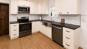 A modern kitchen with white cabinetry, a stainless steel microwave, oven, and dishwasher, and a wooden floor. - Five Arrows Lakehouse With Dock (Rocky Mount)