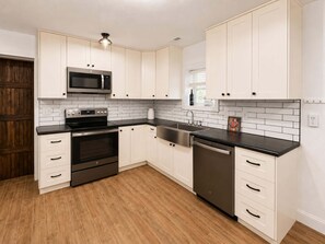 A modern kitchen with white cabinetry, a stainless steel microwave, oven, and dishwasher, and a wooden floor. - Five Arrows Lakehouse With Dock (Rocky Mount)