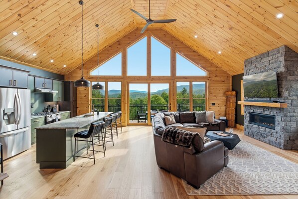Ein geräumiges Loft mit hohen Decken, einer Küche mit modernen Geräten, einer gemütlichen Sitzecke mit Kamin und großen Fenstern mit Blick ins Freie.