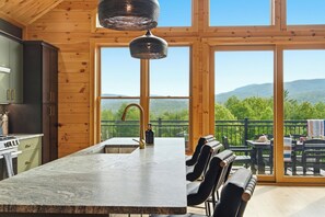 Eine Küche mit einer großen Kochinsel, ein Essbereich mit Sitzgelegenheiten im Freien und ein Blick auf die Berge durch große Fenster.