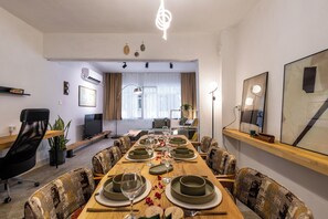 A dining area with a long table set for a meal, surrounded by patterned chairs, with a television and artwork on the walls.