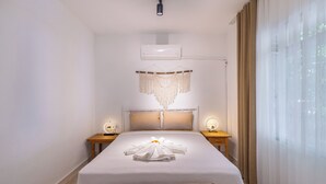 Een hotelkamer met een bed, nachtkastjes, een bankje, een airconditioning en een raam met gordijnen.