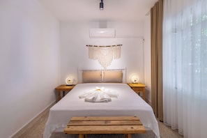 Een hotelkamer met een bed, nachtkastjes, een bankje, een airconditioning en een raam met gordijnen.