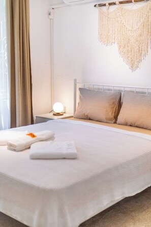 A neatly made bed with a white comforter, two pillows, and a folded towel with an orange flower.