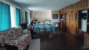 A living room with a sofa, a dining table with chairs, a kitchen area, and wooden paneling on the walls. - Spacious Family-Friendly Kings Park Retreat Sleeps 6+ 3BR/3BA A/C, WiFi & Parkin (Belize City)