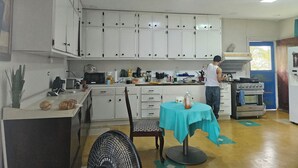 A compact kitchen with white cabinets, a dining area with a table and chairs, and a person cooking at the stove. - Spacious Family-Friendly Kings Park Retreat Sleeps 6+ 3BR/3BA A/C, WiFi & Parkin (Belize City)