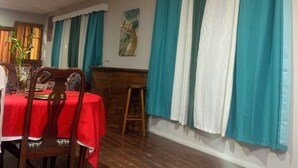 A dining area with a red tablecloth, wooden chairs, and teal curtains. - Spacious Family-Friendly Kings Park Retreat Sleeps 6+ 3BR/3BA A/C, WiFi & Parkin (Belize City)