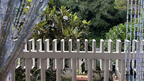 A white fence with vertical slats, a garden with various plants, and a clear blue sky. - Cozy, quiet for families. Pets allowed (Perugia)