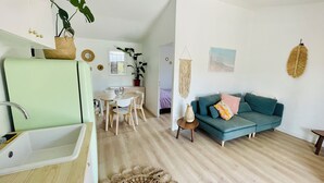 Ein modernes Wohnzimmer mit einem türkisfarbenen Sofa, einer Essecke mit weißem Tisch und Stühlen sowie einer Küche mit einem grünen Spülbecken.