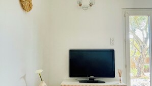 Ein modernes Wohnzimmer mit einem Flachbildfernseher auf einer Holzkommode, einem kleinen runden Tisch mit einer Vase und einer Wanddekoration.