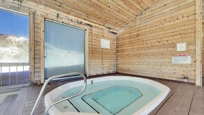 Een houten wellnessruimte met een bubbelbad, houten wanden en een glazen deur.