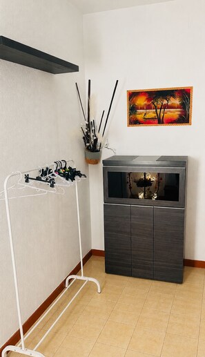 Ein Zimmer mit einem dunklen Holzschrank, einem weißen Wäscheständer, einem Sonnenuntergangsgemälde und einer Vase mit dekorativen Zweigen.