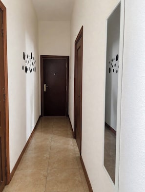 Ein Korridor mit Fliesenboden, einer dunklen Holztür und einer Wand mit kreisförmigen Mustern.