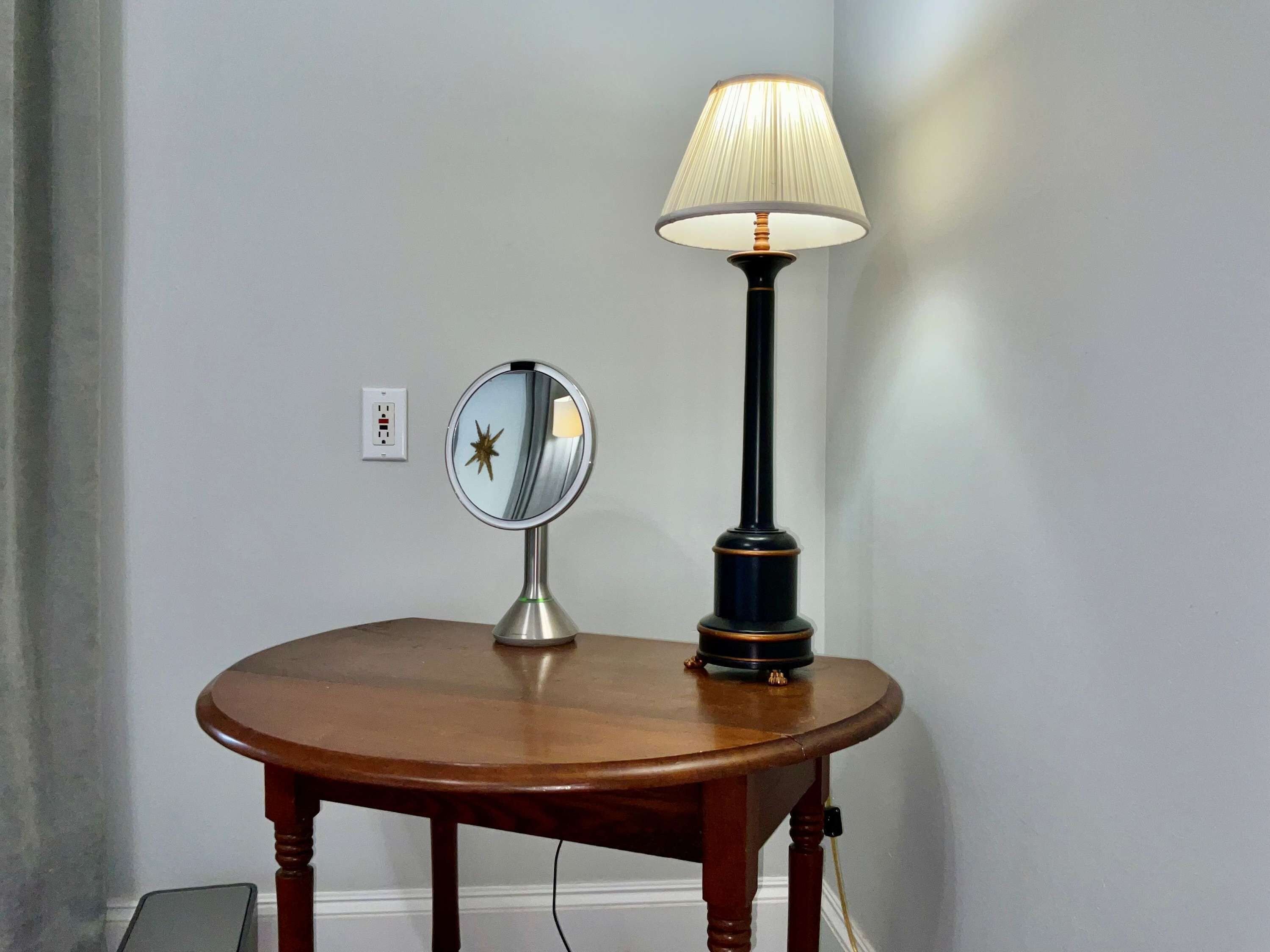 Een ronde houten tafel met een spiegel en een lamp.