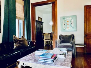Ein Wohnzimmer mit einer Ledersofa, einem Marmortisch mit Büchern, einem Holzstuhl und einem Gemälde an der Wand.