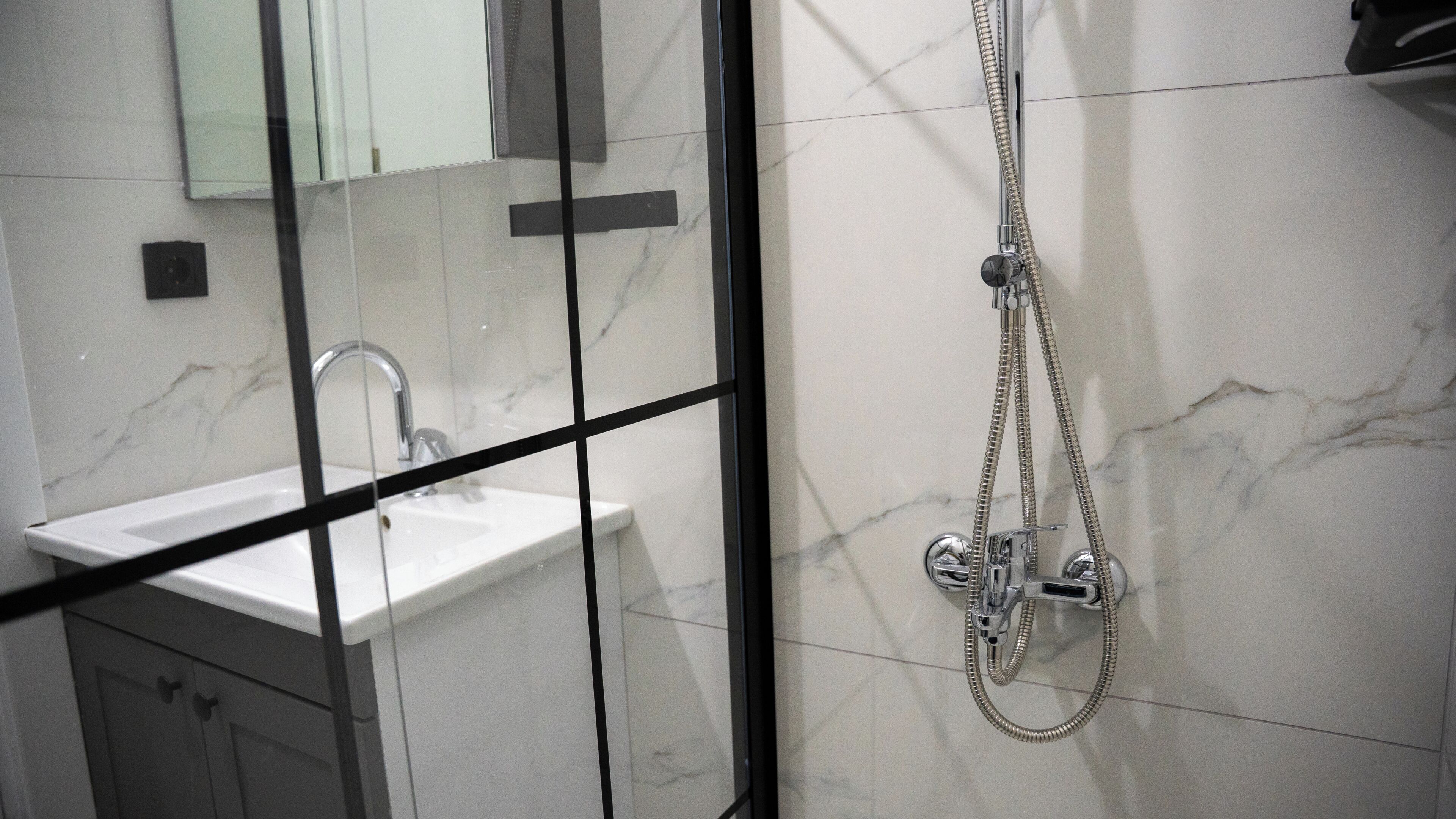 A bathroom with a glass partition, a sink, and a shower with a handheld showerhead.