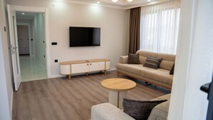 A modern living room with a sofa, a small round table, a TV mounted on the wall, and a wooden cabinet. - Santana Suit (Arsin)