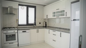A kitchen with white cabinets, a stove, a dishwasher, and a window with blinds. - Santana Suit (Arsin)