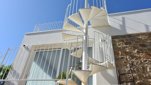 A spiral staircase leading to a balcony with a stone wall and a metal railing.