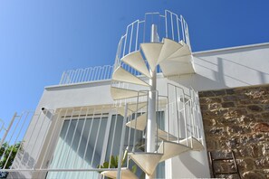 A spiral staircase leading to a balcony with a stone wall and a metal railing.
