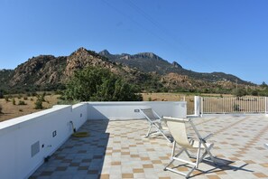 Una terraza en la azotea con piso a cuadros, dos sillones de descanso y vistas a un paisaje montañoso.