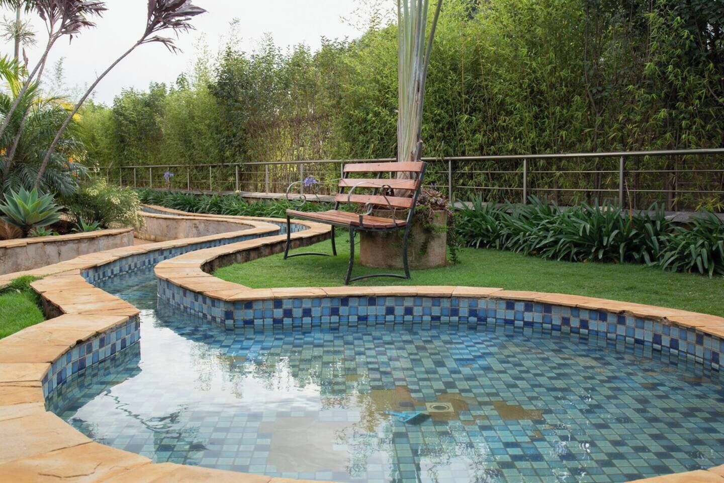 Ein Schwimmbecken mit gefliesten Rändern, umgeben von einem Garten mit verschiedenen Pflanzen und einer hölzernen Bank.