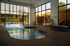 Ein Pool mit gewölbter Kante, großen Fenstern und Liegestühlen.