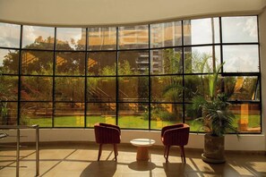Ein Zimmer mit großem Fenster, zwei Stühlen, einem kleinen Tisch und einem Blumentopf.