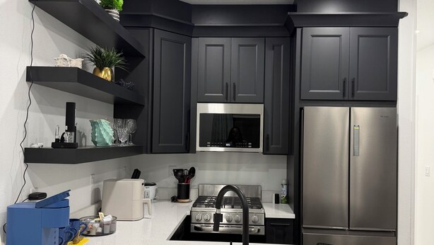 A modern kitchen with dark cabinets, a stainless steel refrigerator, a microwave, and a gas stove.