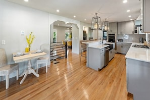 A modern kitchen with a central island, wooden flooring, and pendant lighting.
