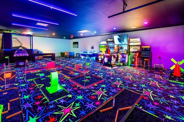 A room with arcade games, a star-patterned carpet, and neon ceiling lights.