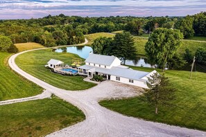 A large white house with a swimming pool, surrounded by a well-maintained lawn and a curved driveway.