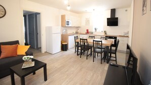 A modern kitchen with a dining area, a black TV, and a clock on the wall. - Les Loges de Véro RDC - 5 min from Verdun, private parking, motorcycle garage, air conditioning. (Thierville-sur-Meuse)