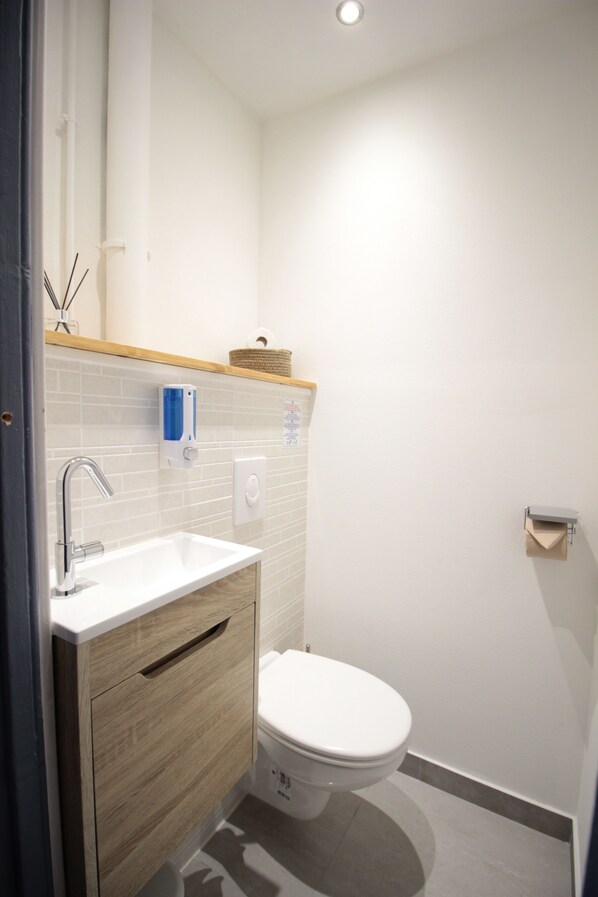A bathroom with a white sink, wooden vanity, and a toilet. - Les Loges de Véro, Ground Floor — 5 min. from Verdun, private parking, motorcycle garage, air conditioning. (Thierville-sur-Meuse)