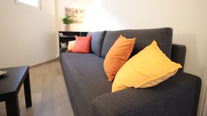 A living room with a dark grey sofa, two orange and one yellow pillow, a black coffee table, and a small plant on a side table.