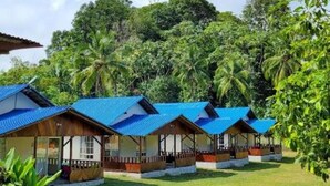 A row of blue-roofed cabins with a grassy lawn and dense tropical foliage in the background.