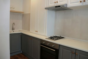 Eine Küche mit grauen Schränken, einer weißen Arbeitsplatte, einem Gasherd und einem eingebauten Backofen.
