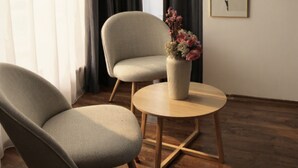 A room with a wooden floor, a grey armchair, a round wooden table with a vase of flowers, and a framed picture on the wall. - Mosilor Residence (București)