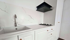 A kitchen with a white marble backsplash, a stainless steel sink, a gas stove, and white cabinetry with wooden knobs. - Mosilor Residence (București)