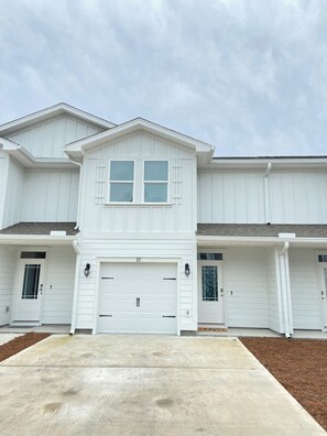 A two-story building with a central garage door, two side doors, and a small porch area. - San Destin Dream Vacation 3-bedroom townhome in beautiful Santa Rosa Beach. (SANTA RSA BCH)