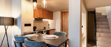 A dining area with a table set for four, wooden chairs, a modern pendant light fixture, and a staircase leading to an upper level.
